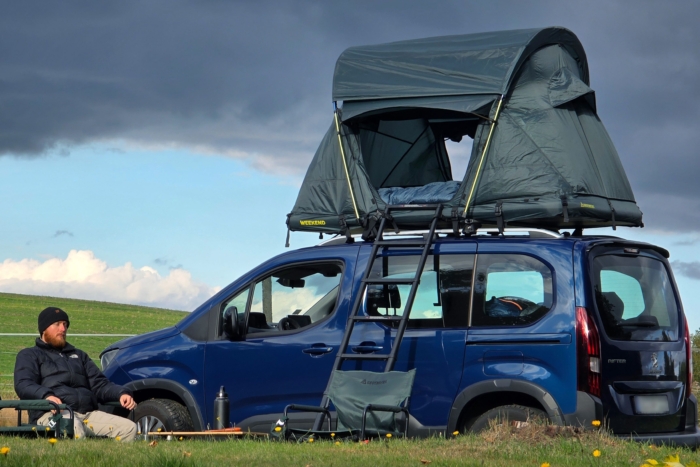 Person sits in camp chair next to car with rooftop tent