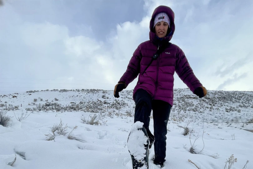 Hiker in a purple jacket walking uphill through snow-covered terrain