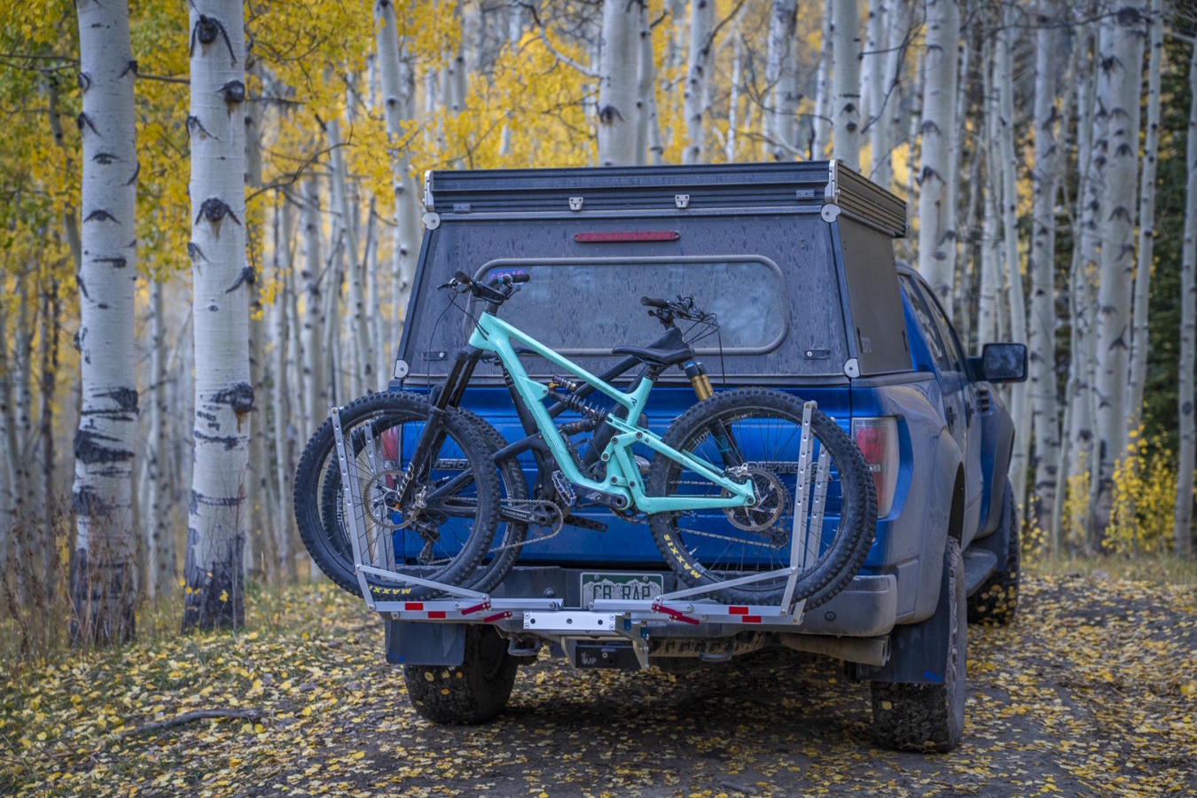 A 1UP USA heavy duty bike rack mounted on the back of a blue truck, securely holding a mountain bike