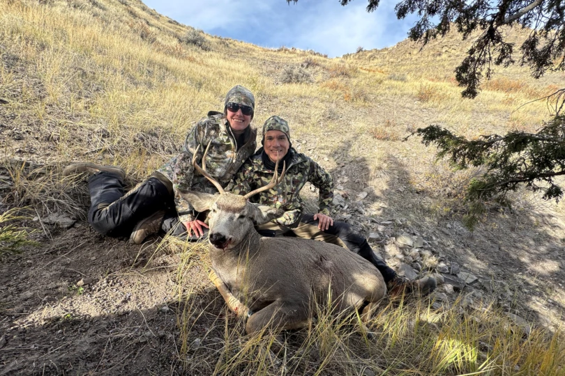 Two hunters wear AllClima hunting jackets while posing beside a harvested deer
