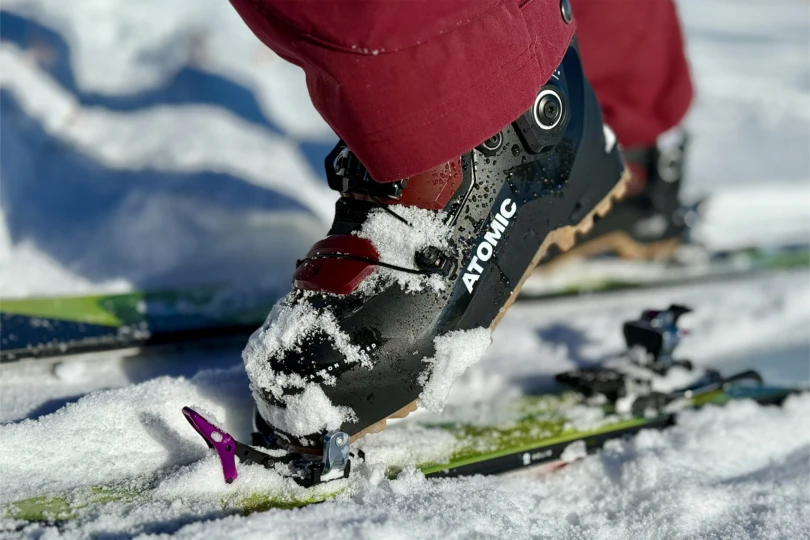 The boot stepping into tech bindings with snow packed around the toe