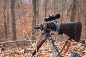 A hunting rifle mounted on the BOG Bantam Deathgrip Tripod overlooking wooded, hilly terrain.