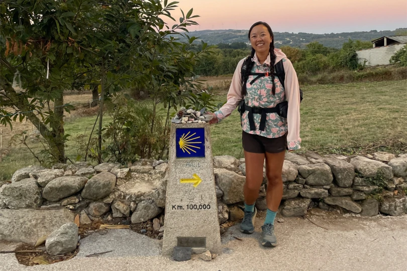 A pilgrim stands beside the 100 km stone marker on the final stretch of the Camino route