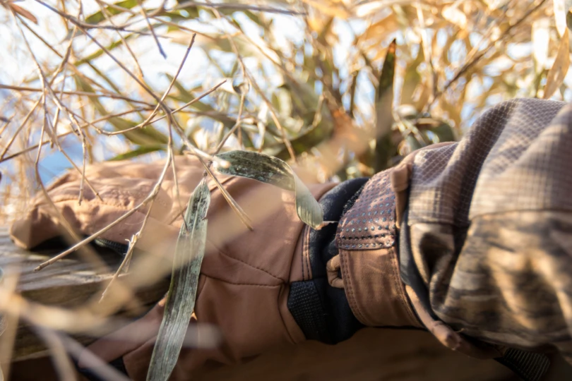 A gloved hand on a duck blind shelf surrounded by brush.