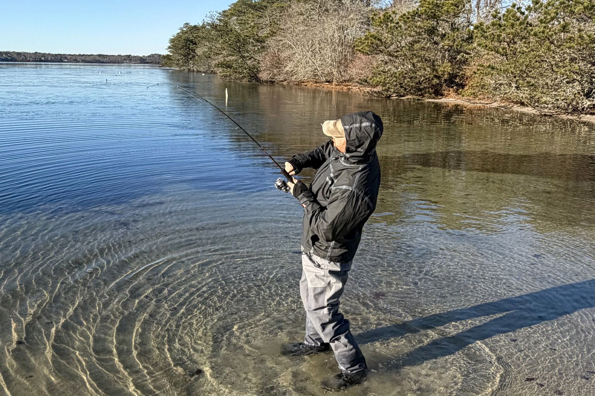 A fisherman wearing the Columbia PFG Force XII™ ODX Jacket and Bib while fishing in clear, shallow water near the shoreline