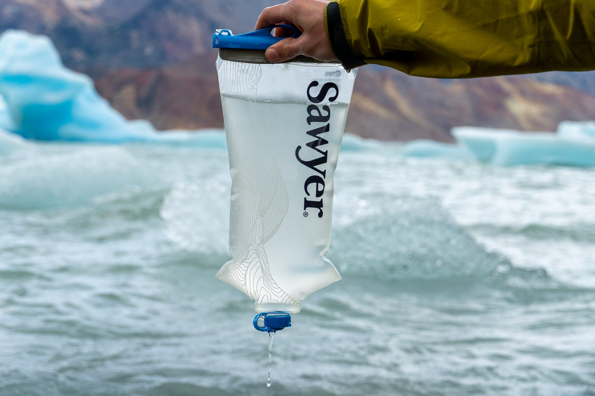 the author holds the cnoc/sawyer bladder filled with water in front of a glacial-ice-filled bay in patagonia