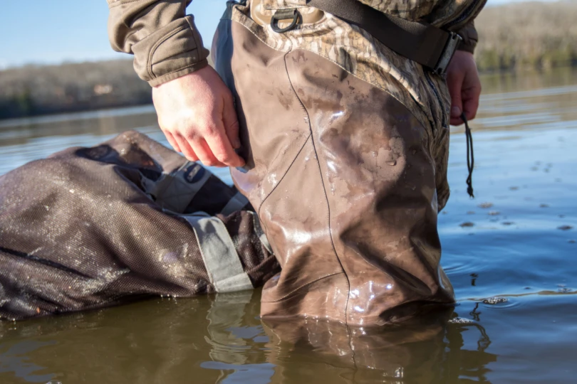 The seams on the Drake Waterfowl Guardian Elite HND Front Zip Waders submerged in water with a bag of decoys in the background.