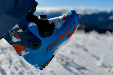 The touring boots stand in fresh snow with bright blue shells and orange details