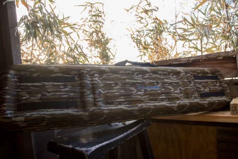 The Plano Diverge Gun Case propped up in a duck hunting blind with a sunrise through brush behind it.