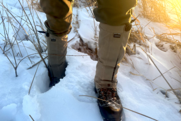 The Kings Camo XKG Leg Gaiter on a hunters legs in front of a snowy landscape with the sunset in the background.