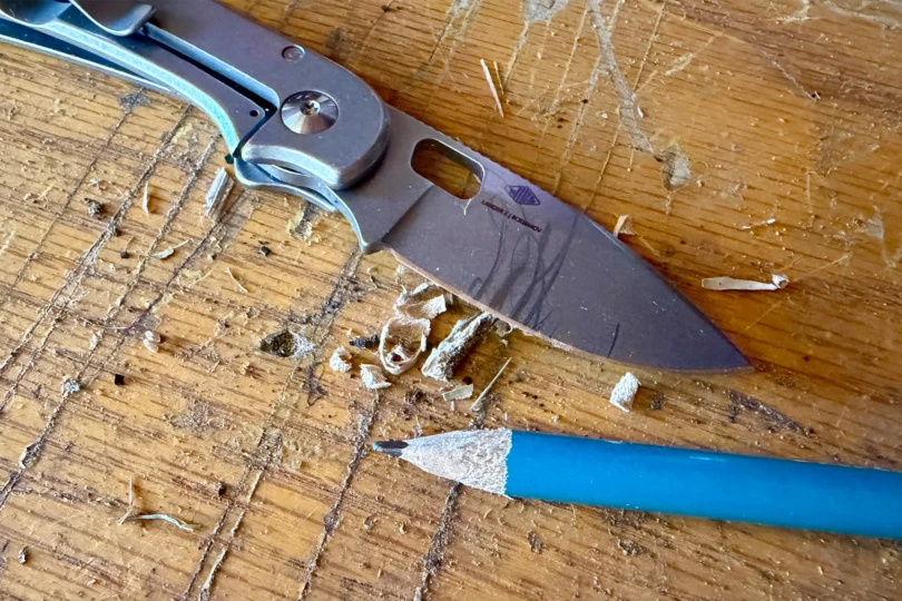 The knife after carving wood curls beside a sharpened pencil