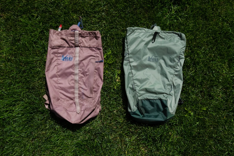 two flash 18 daypacks lay on a grass lawn, one is mauve and one is green