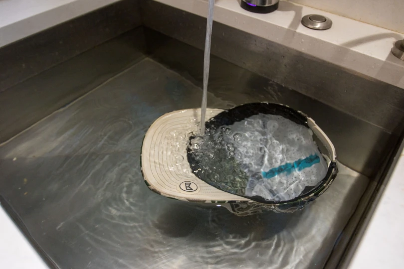 The Melin Odysea Stacked Hydro Hat floating in a kitchen sink with water pouring on it.