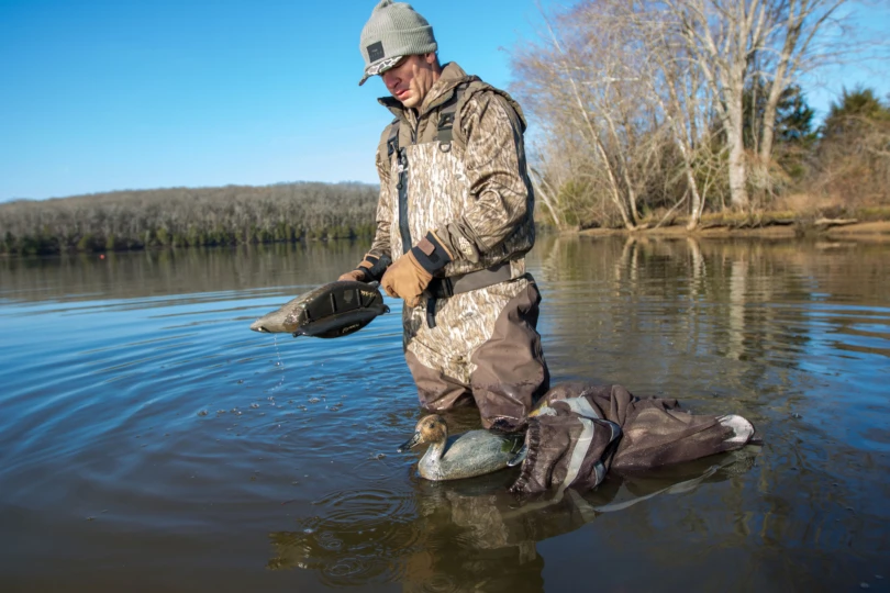 A duck hunter picking up decoys in the water.