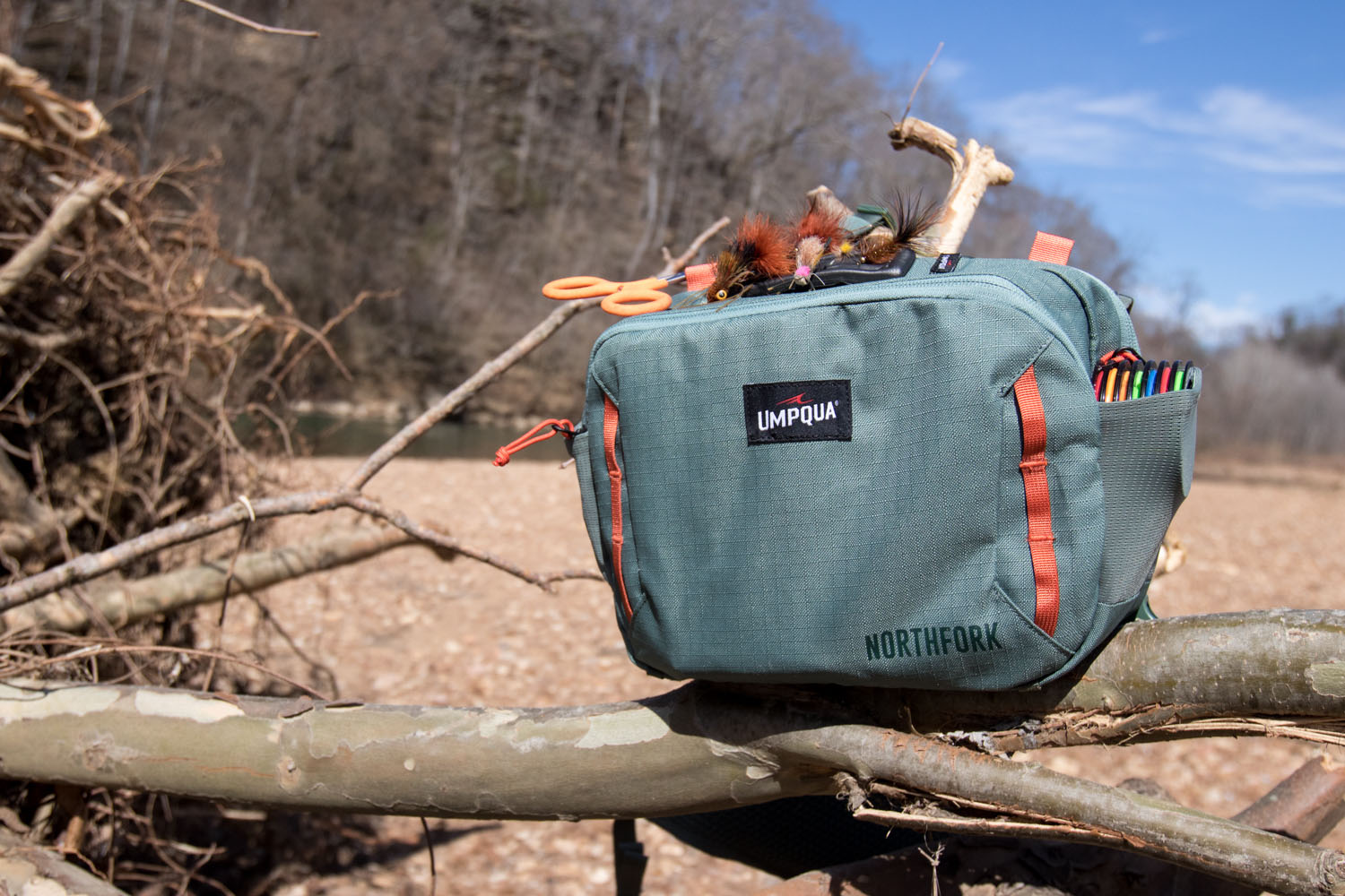 A fishing pack rests on driftwood. A river flows in the background