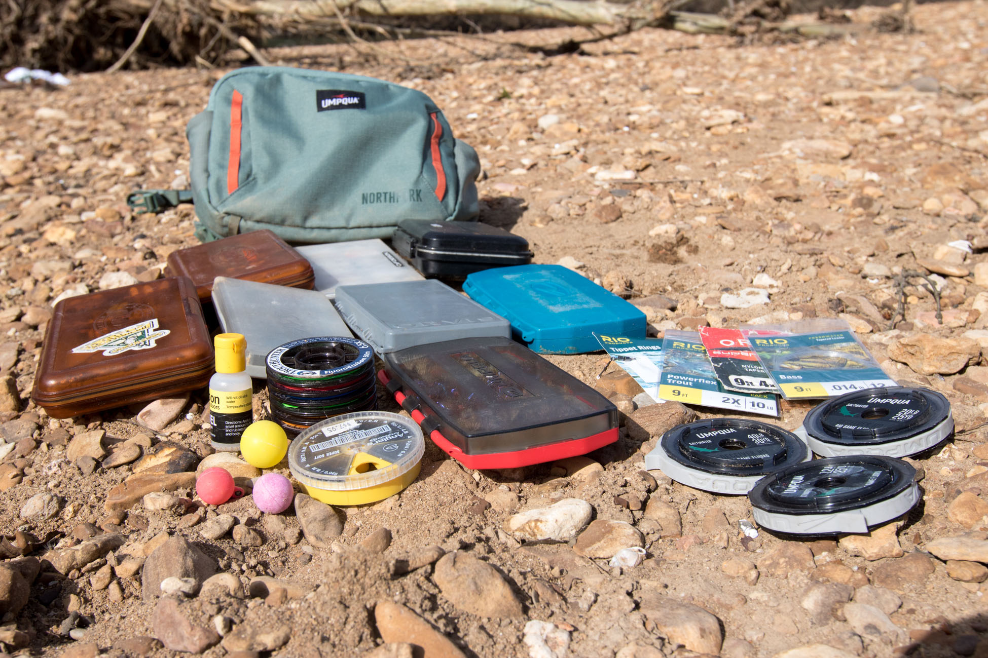 Fly boxes and other fly fishing tools scattered in front of an opened pack.