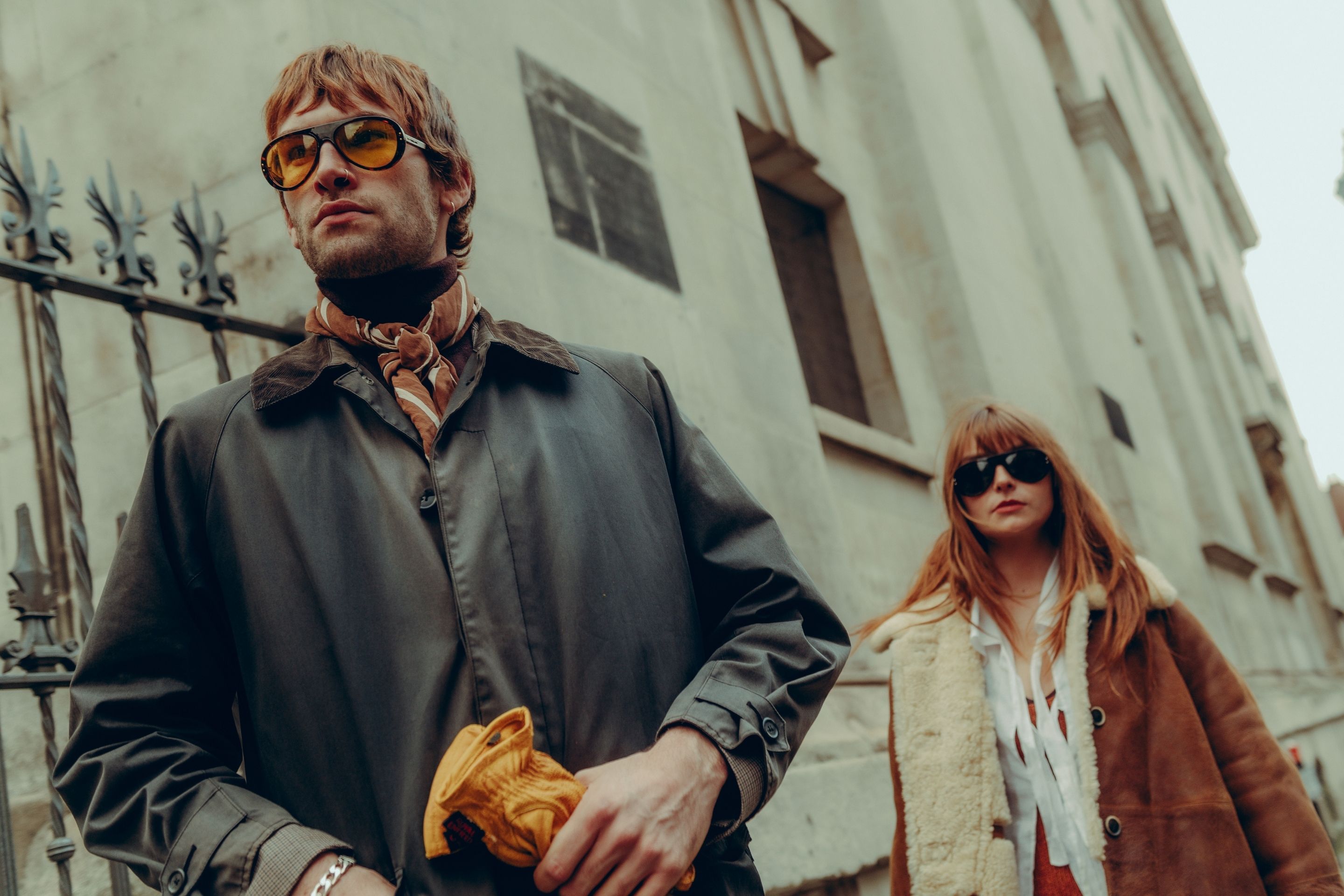 Man and woman walk down street wearing sunglasses