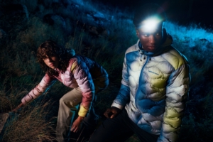 Man and woman walk through field at night in colorful jackets
