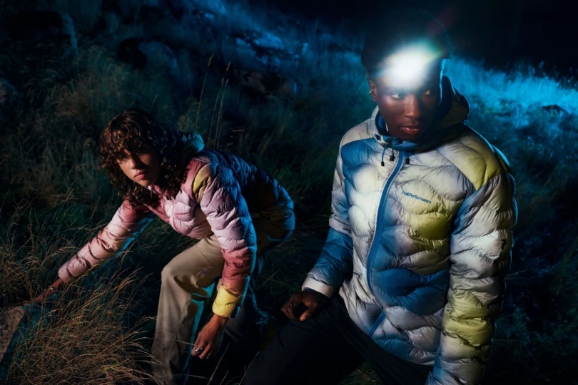 Man and woman walk through field at night in colorful jackets