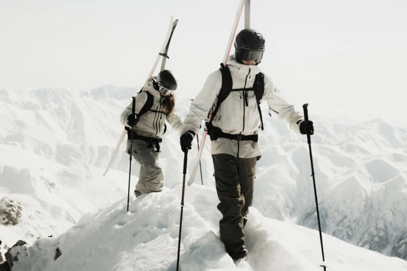 Two people hike up snowy mountain carrying skis