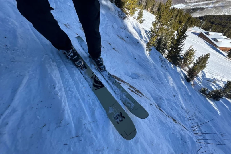 Revolt skis stand upright in the snow near ski poles and a trail edge