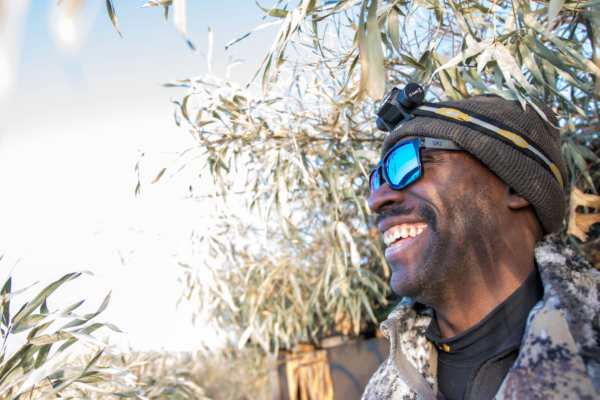 A duck hunter in a blind, wearing the Wiley X Apex sunglasses while laughing.