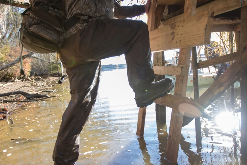 A hunter climbing into an elevated duck blind wearing a set of the best duck hunting waders of 2026.