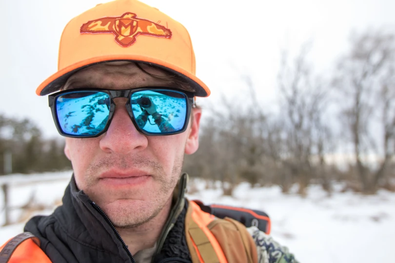A close up shot of a hunters face wearing sunglasses and an orange hat.