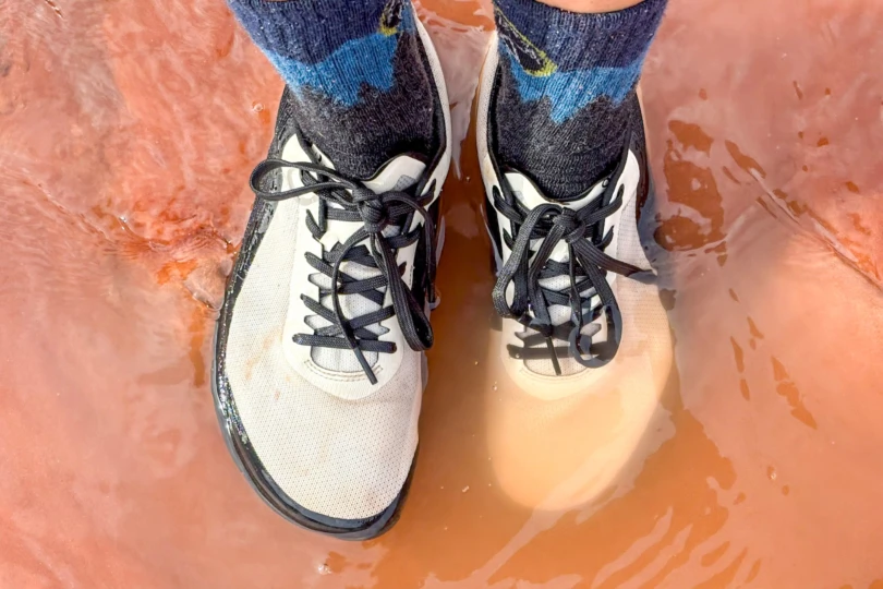 The Yama shoes standing in shallow water on a muddy trail