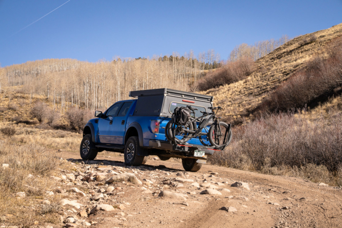 The truck drives a rocky road with two bikes mounted on the rack