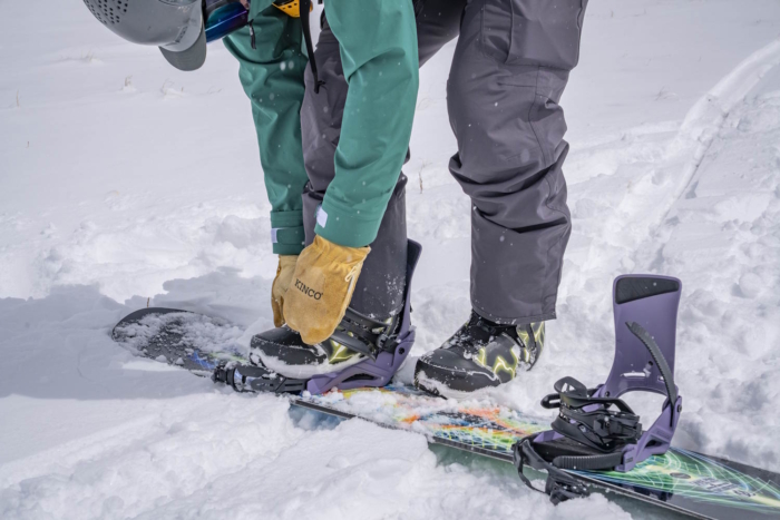 A snowboarder adjusting snowboard bindings in the snow