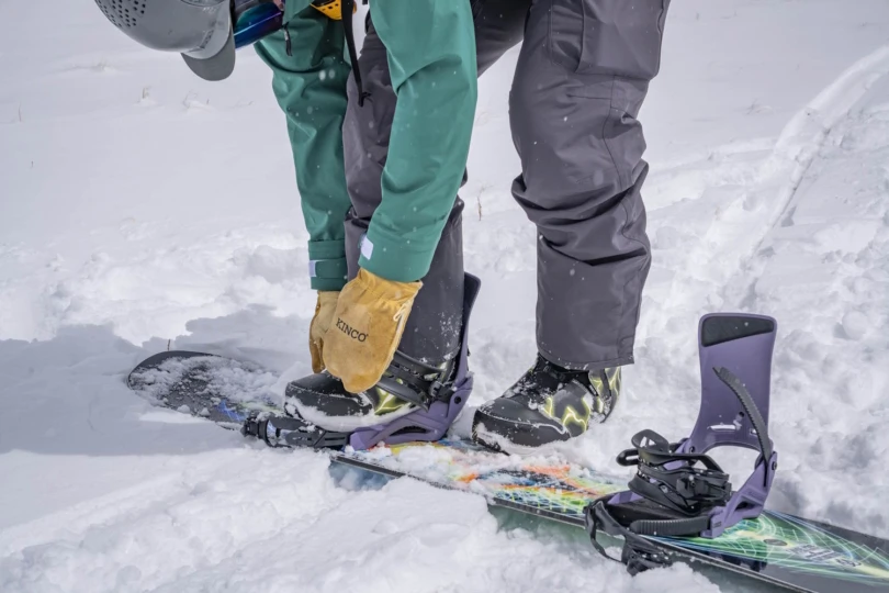 A snowboarder adjusting snowboard bindings in the snow