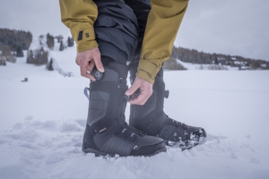 Snowboarder tightening BOA dials on black snowboard boots while standing in the snow
