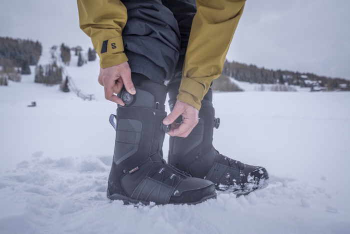 Snowboarder tightening BOA dials on black snowboard boots while standing in the snow