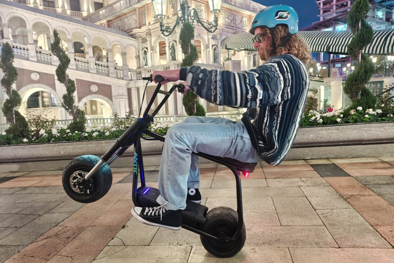 A rider sits low on the Future Motion Antic eBike while riding on a paved city plaza at night