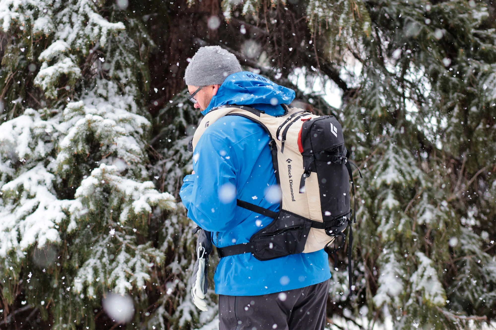Side view of a skier wearing the Black Diamond Dawn Patrol 25 Pack while standing in a snowy forest