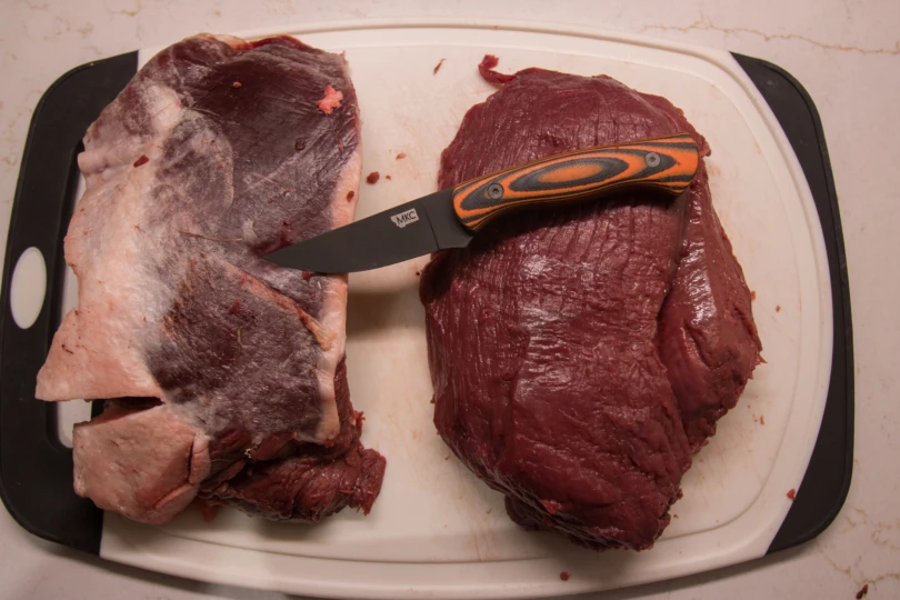A knife laying on two cuts of meat on a cutting board.
