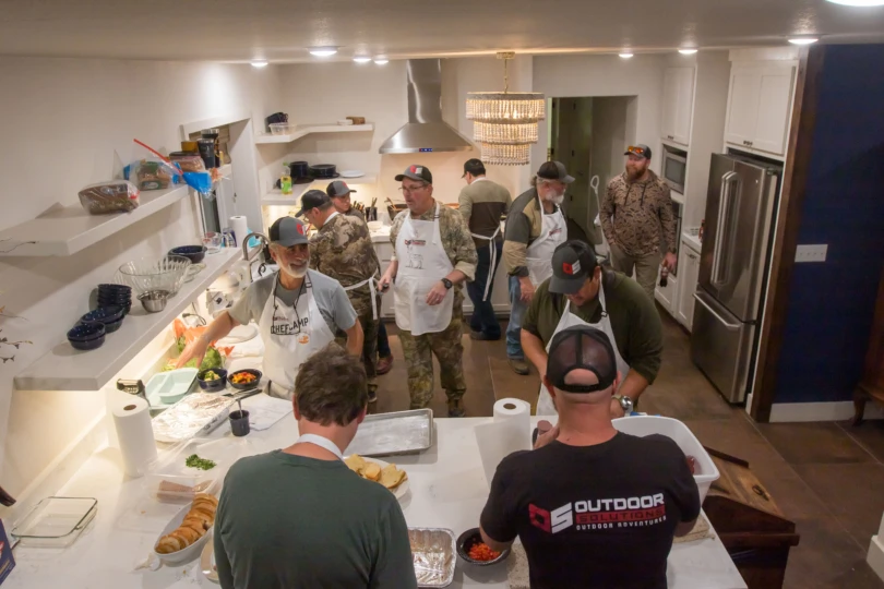 A crew of people cooking in a kitchen at a field to table experience with Outdoor Solutions