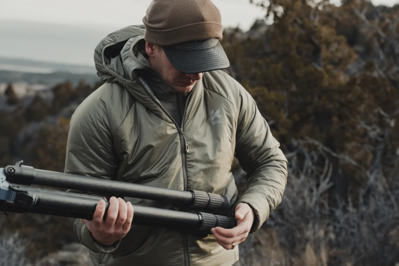 A hunter wearing the new Kifaru Pointe Synthetic Puffy Jacket putting away a tripod