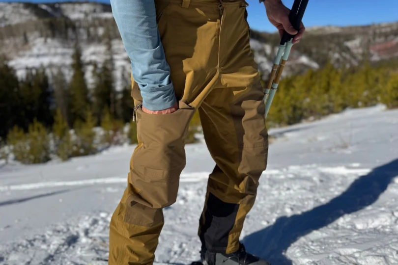 Side view of the Emiko pants highlighting the zippered thigh pocket while standing on snow
