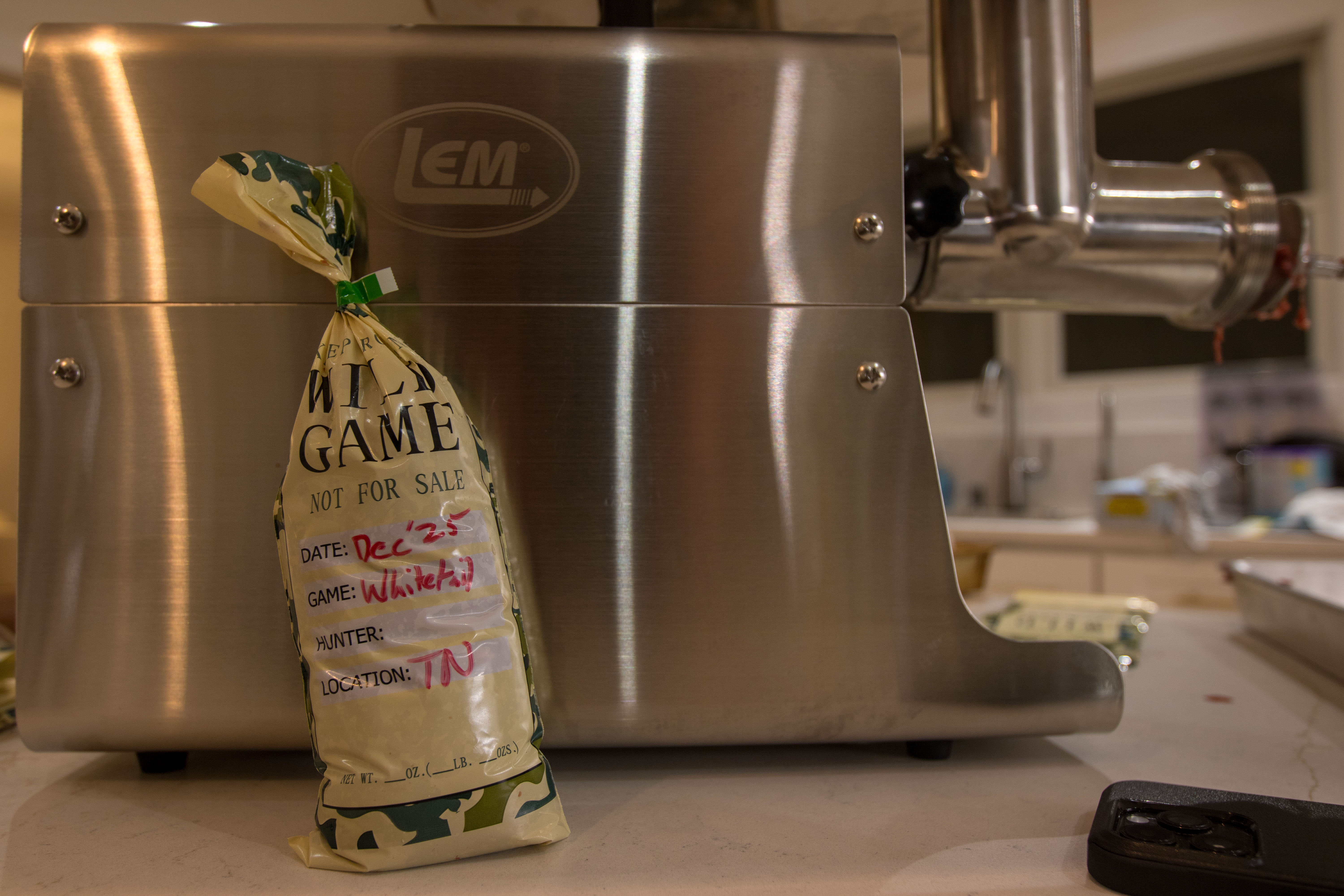 A package of wild game meat leaned up against a LEM meat grinder.