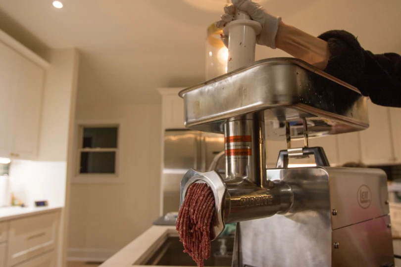 Ground meat coming from the LEM Big Bite #22 1.0 HP Meat Grinder in a kitchen.