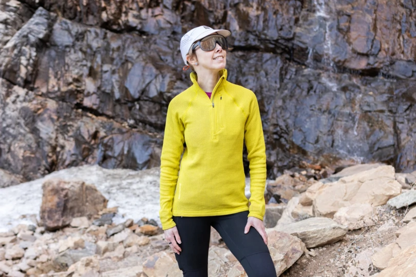 Houdini Pace Flow Half Zip worn by a person standing on rocks near flowing water