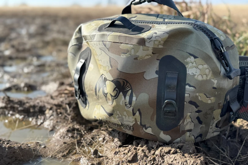 KUIU DeltaStorm 800 Submersible Waistpack resting on muddy ground near shallow water