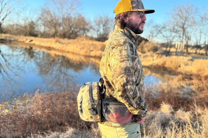 Person wearing the KUIU DeltaStorm 800 Submersible Waistpack beside water