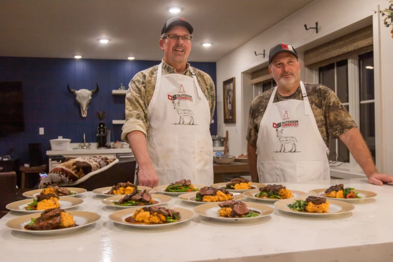 Two hunters, standing over a dish they prepared for dinner.