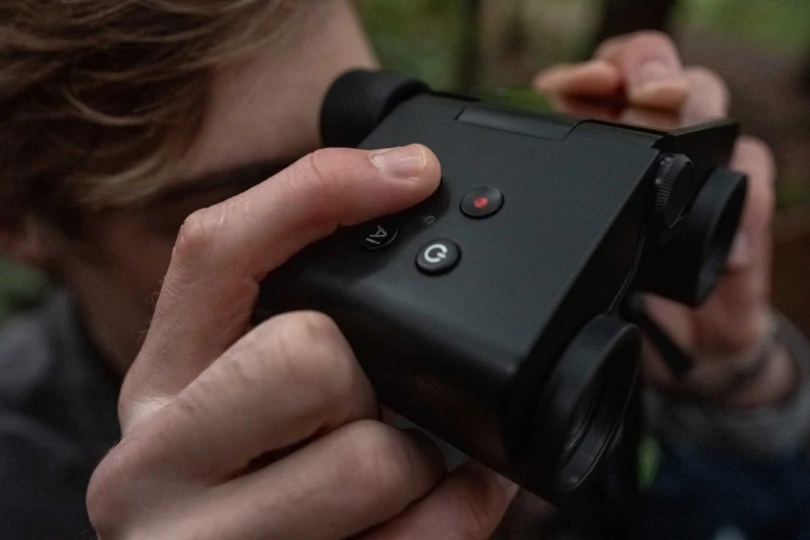 A person using the Solvia ED binoculars, with a close view of the control buttons while looking through them