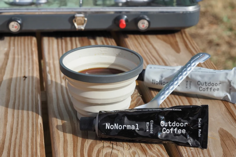 NoNormal coffee tube next to cup and camp stove