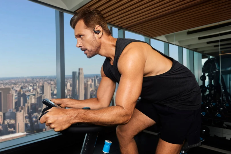 A man wears OpenFit Pro earbuds while exercising on a stationary bike indoors