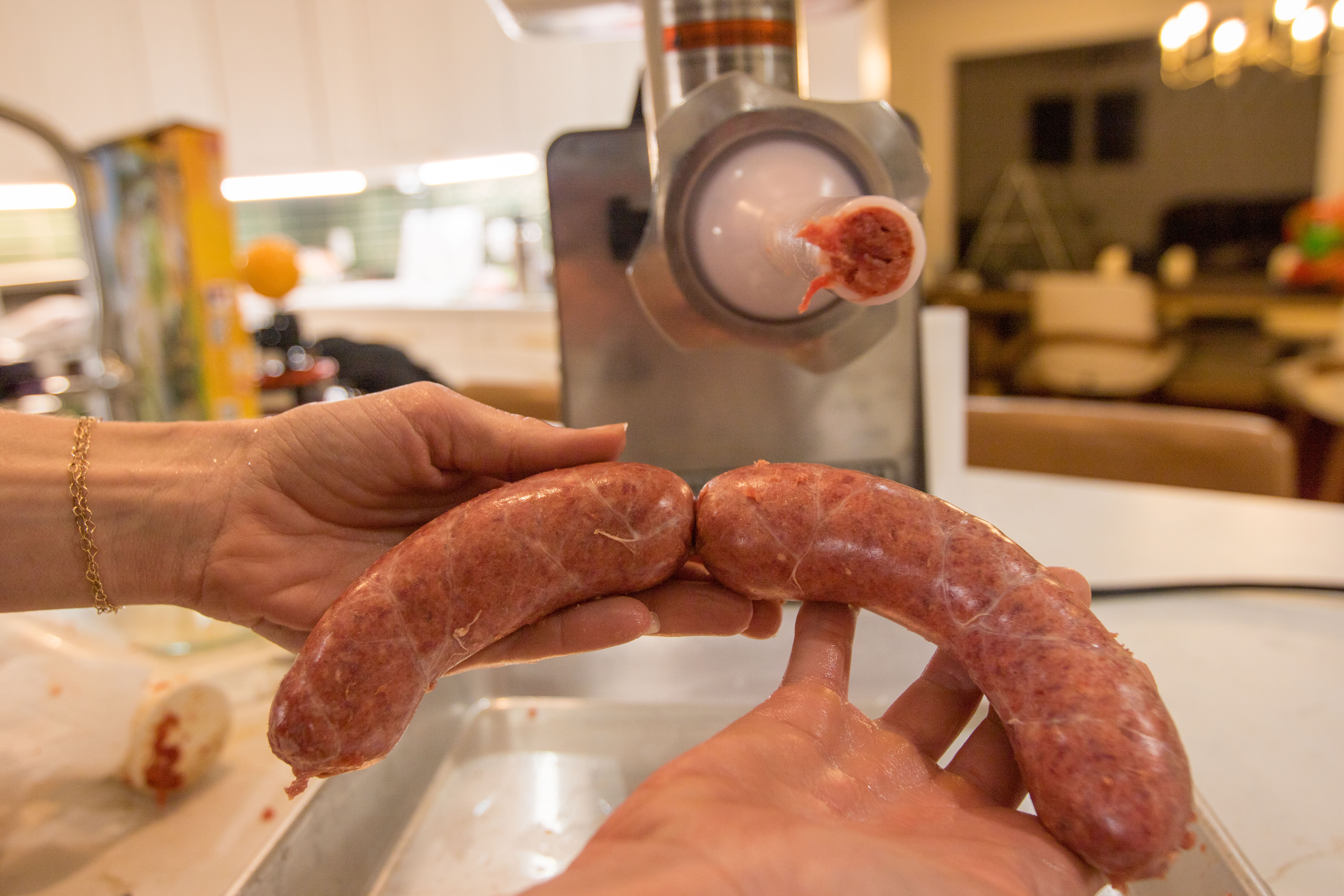 Two brats being held in front of a sausage stuffer.